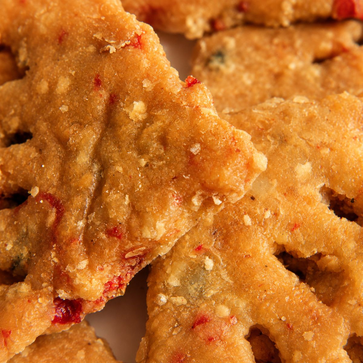 Close-up of golden Njammies Chickpea Peppa Crackers with pieces of Peppadew.